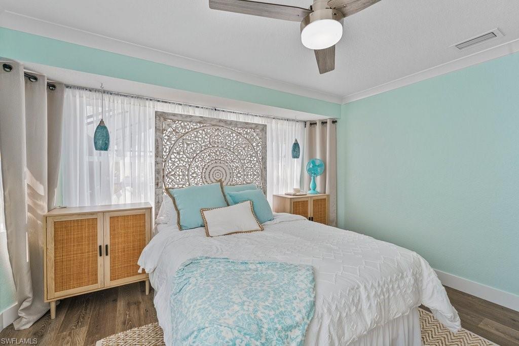 Bedroom featuring light turquoise walls, wood-finish flooring, white crown molding, and a ceiling fan with integrated lighting
