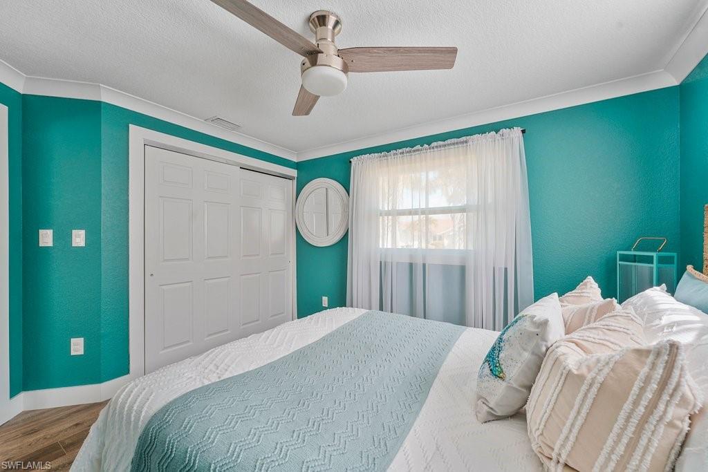 Interior room featuring a ceiling fan, crown molding, wood-finish flooring, sliding closet doors, and a window with sheer curtains