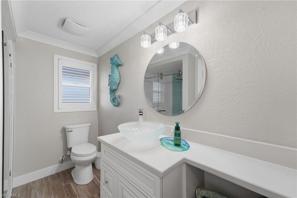 Bathroom with wood-finish flooring, a white vanity with a vessel sink, an oval mirror, and a window with white louvered shutters