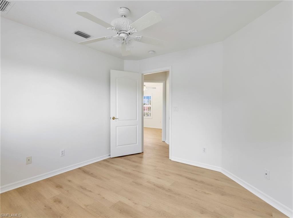 Room featuring wood-finish flooring, white baseboards, a ceiling fan with integrated lighting, and a solid white door with a brass-finish knob