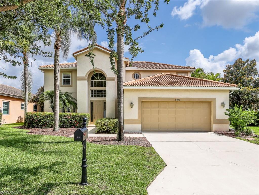 Two-story stucco residence featuring a terracotta tile roof, prominent arched window with grid details, an attached two-car garage, and a concrete driveway