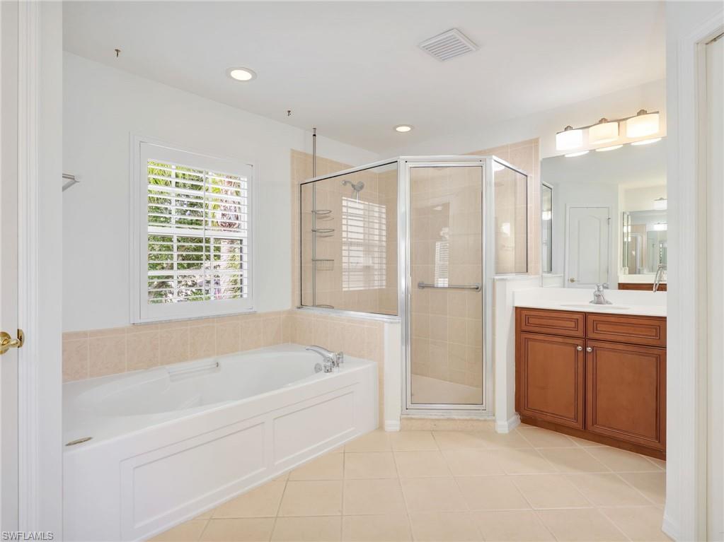 Bathroom featuring a soaking tub, glass-enclosed shower, wood-finish vanity with countertop sink, and tiled flooring