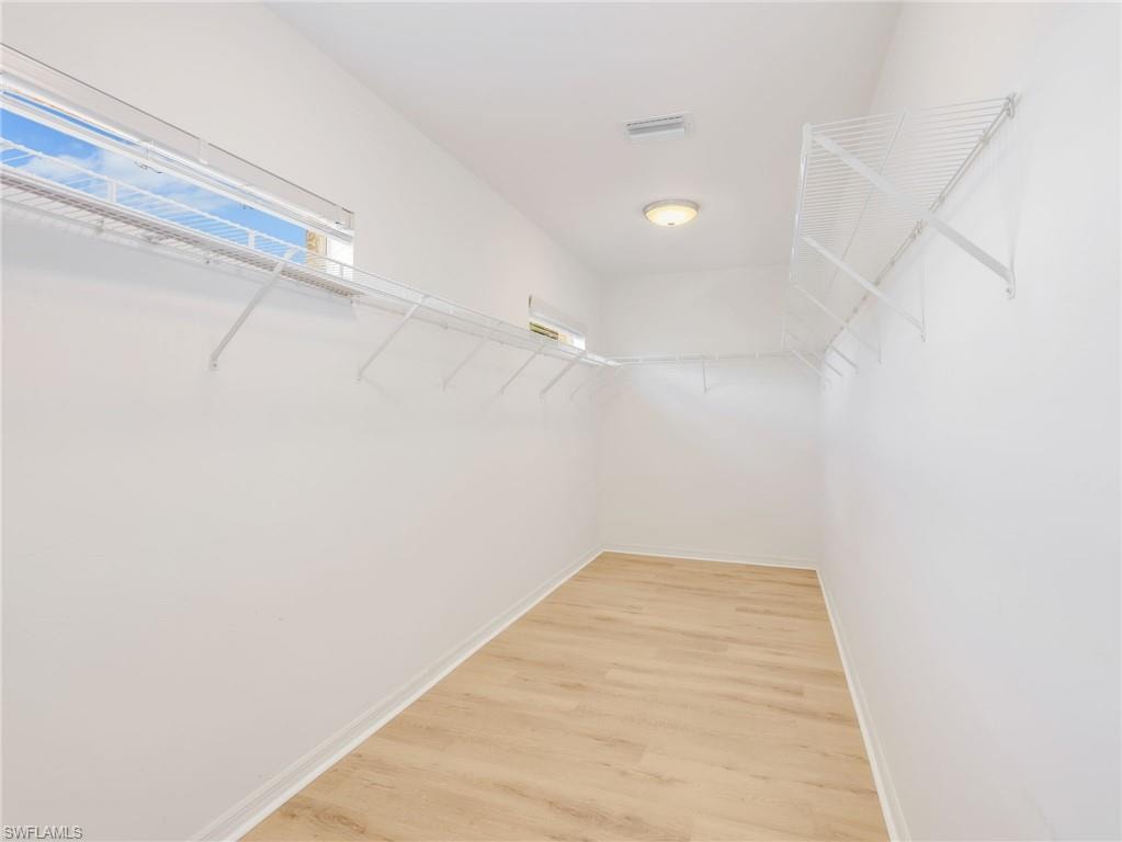 Spacious walk-in closet featuring light wood-finish flooring, white walls, and built-in wire shelving