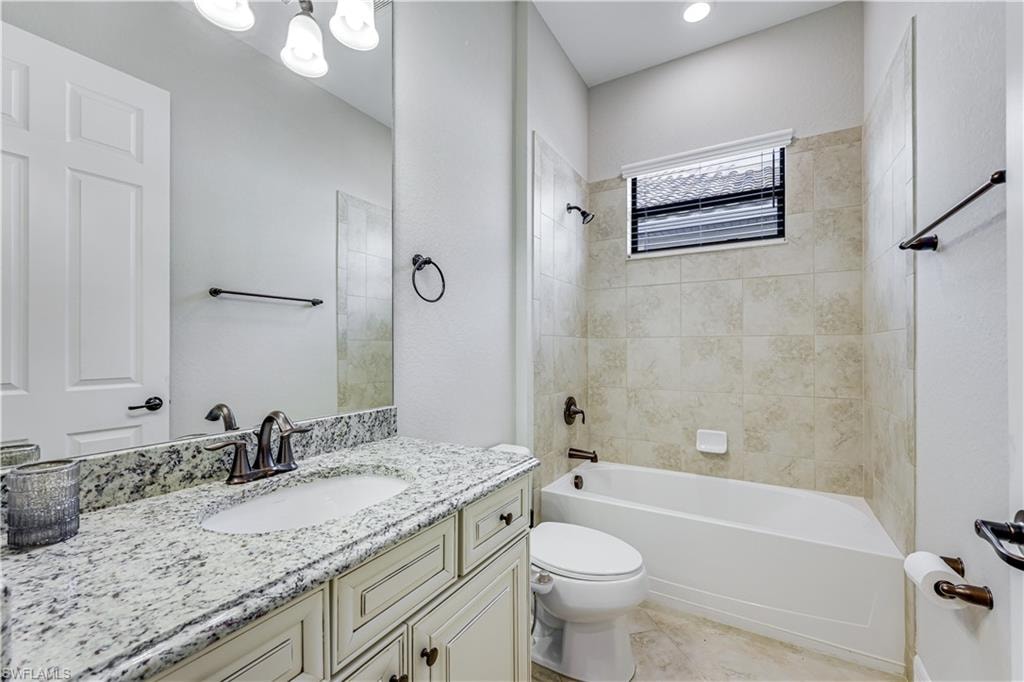 Bathroom featuring a built-in tub with tile surround, a window with blinds, a vanity with a light-colored countertop, and a white paneled door