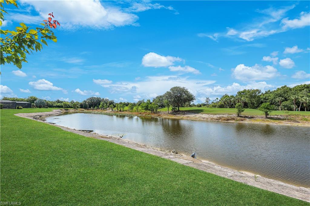 Expansive green lawn bordering a tranquil body of water, with distant treelines and a clear blue sky