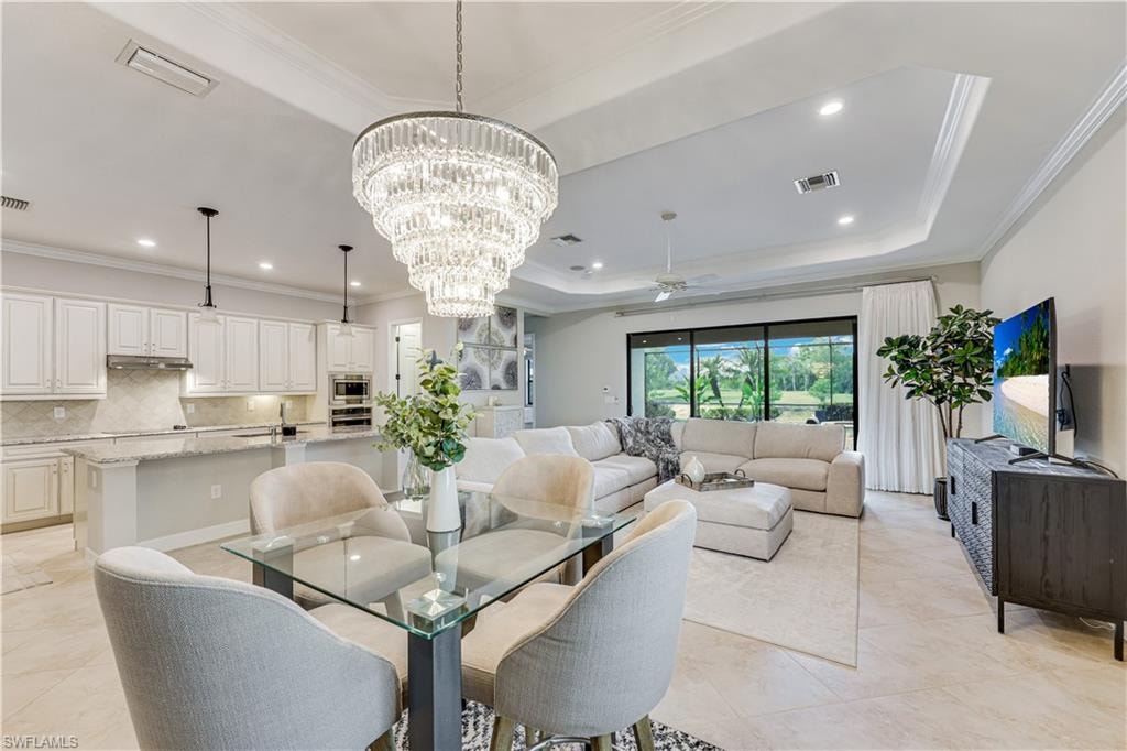 Open-concept living area featuring a large tiered chandelier, tray ceiling with recessed lighting, and expansive sliding glass doors