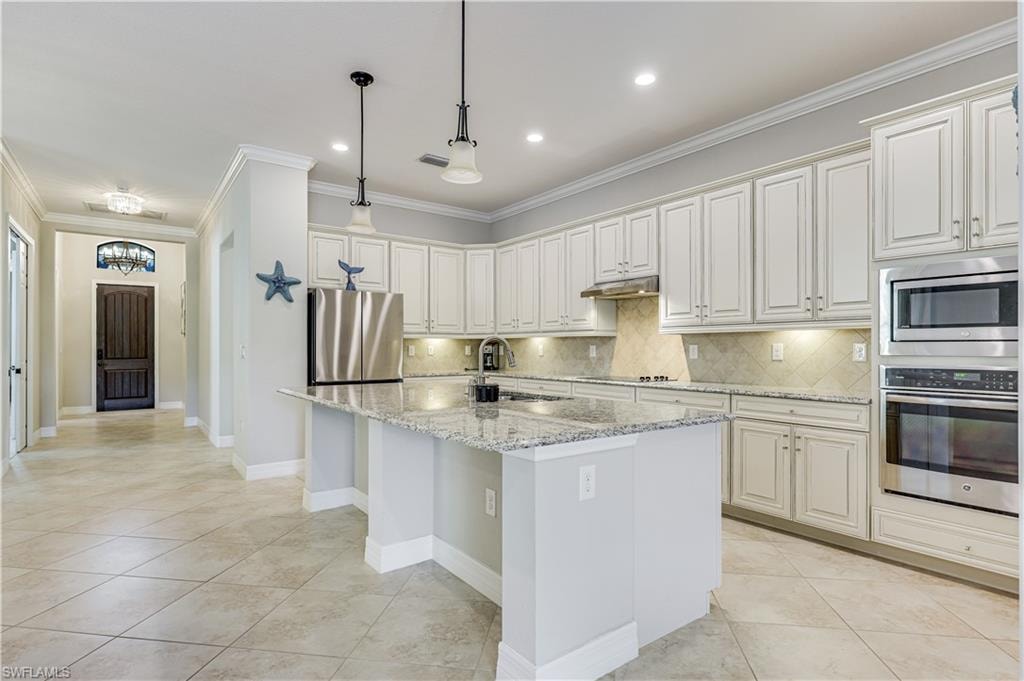 Spacious kitchen featuring an expansive island with granite countertops, abundant white cabinetry, stainless steel appliances, and tile flooring
