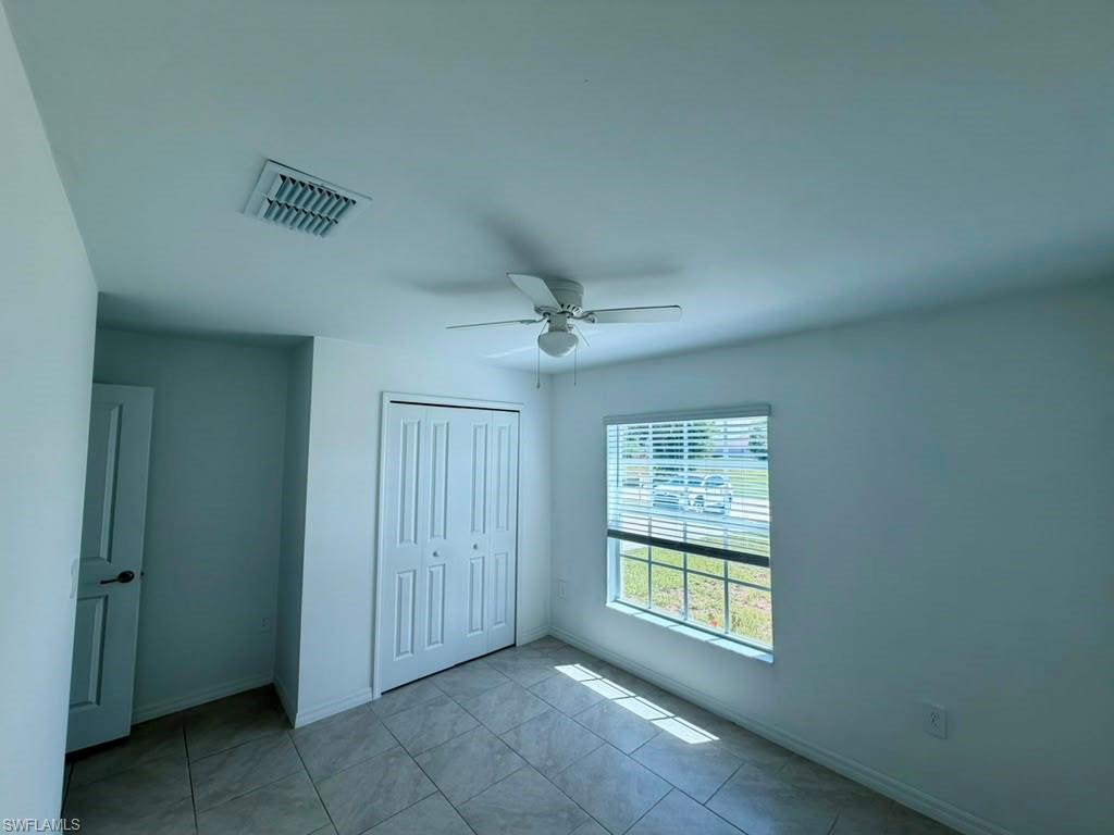 Light-filled room featuring large format tile flooring, a ceiling fan, white bi-fold closet doors, and a window with blinds