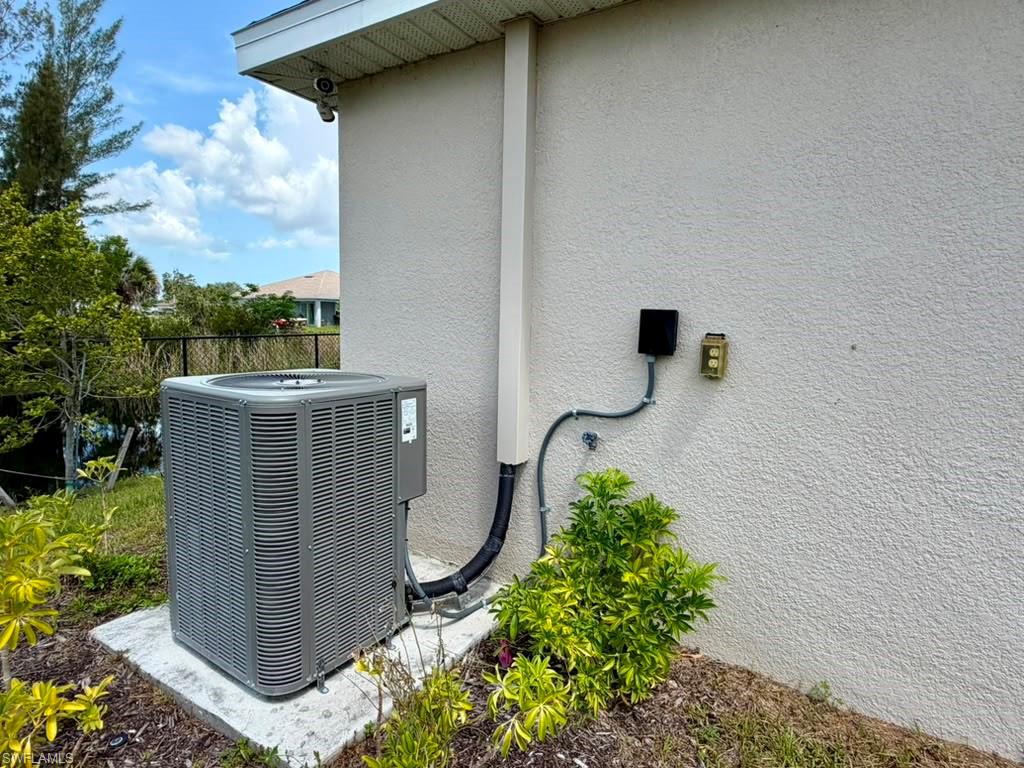 Exterior stucco wall featuring an HVAC condenser unit on a concrete pad with surrounding landscaping