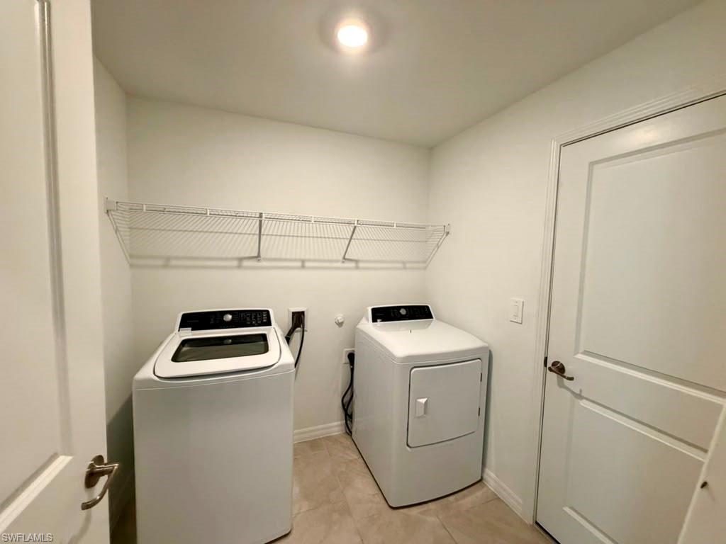 Dedicated laundry area featuring tile flooring, white walls, overhead wire shelving, and an included washer and dryer