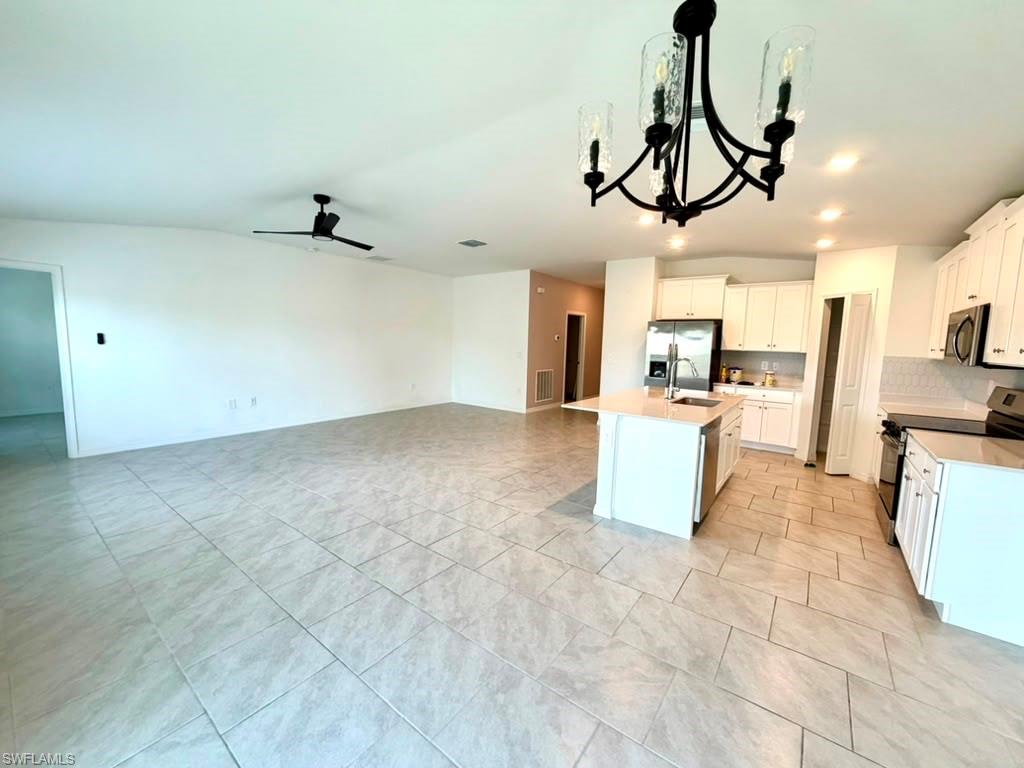 Modern kitchen featuring white cabinetry, stainless steel appliances, a center island with sink, and a tile backsplash