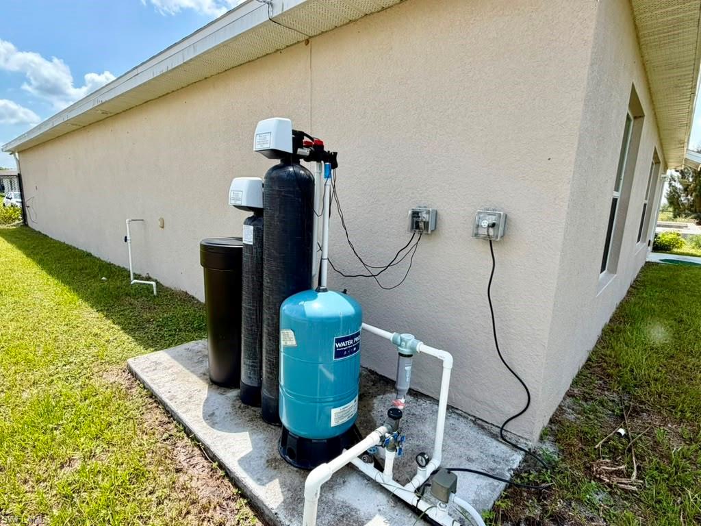 Exterior stucco wall featuring a water filtration system on a concrete pad with visible plumbing