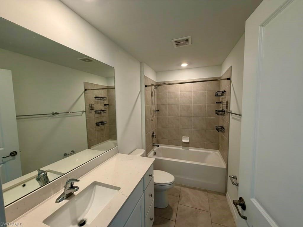 Bathroom featuring a single vanity with an undermount sink and light-toned countertop, a large wall-mounted mirror, a tub/shower combination with tile surround, and tile flooring