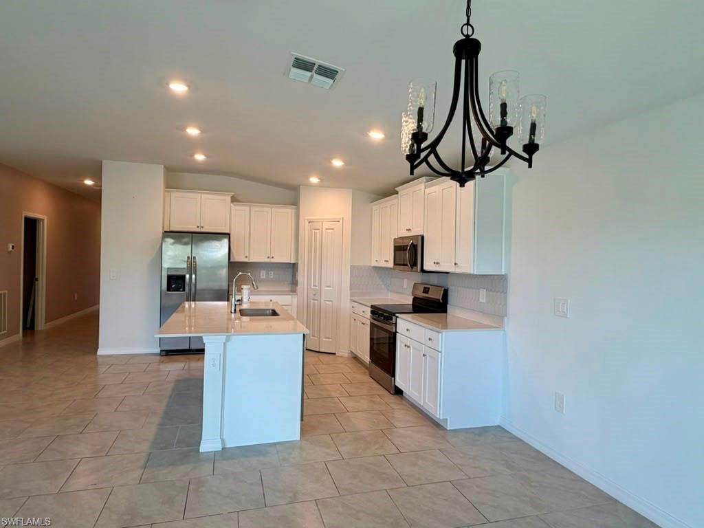 Kitchen featuring a central island, stainless steel appliances, white cabinetry, and a tile backsplash
