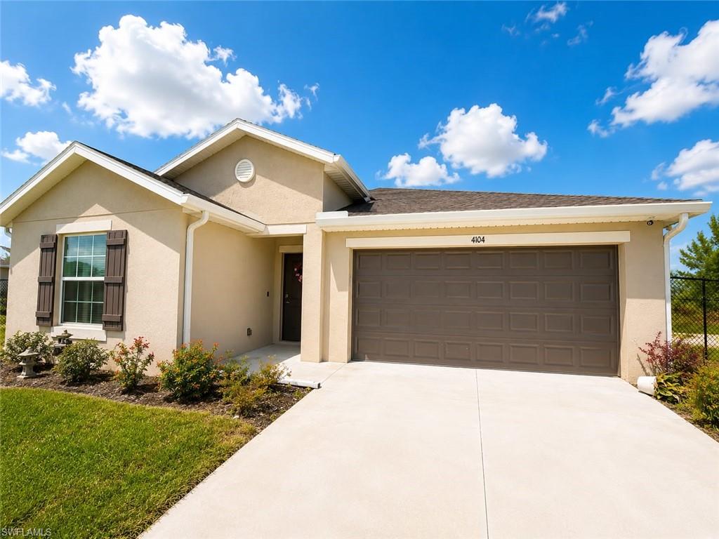 Single-story stucco exterior featuring a two-car garage with a panel door, a concrete driveway, and established front landscaping