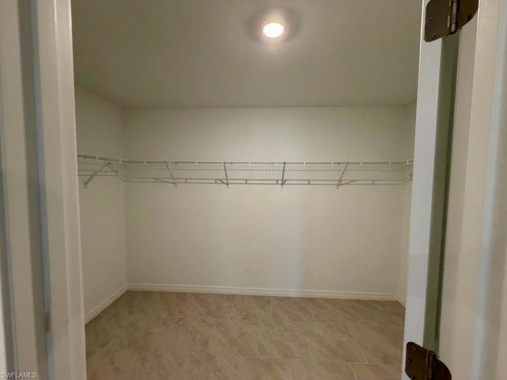 Spacious walk-in closet featuring light-toned tile flooring, white wire shelving, a ceiling-mounted light fixture, and white baseboards