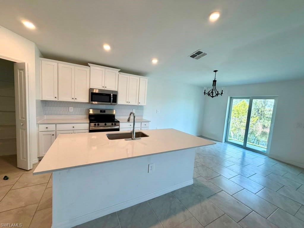 Modern kitchen featuring white cabinetry, stainless steel appliances, a center island with sink, and tile flooring
