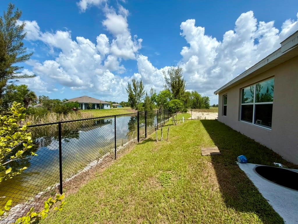 Spacious backyard featuring a black chain-link fence, a waterway, a stucco exterior, and multi-pane windows