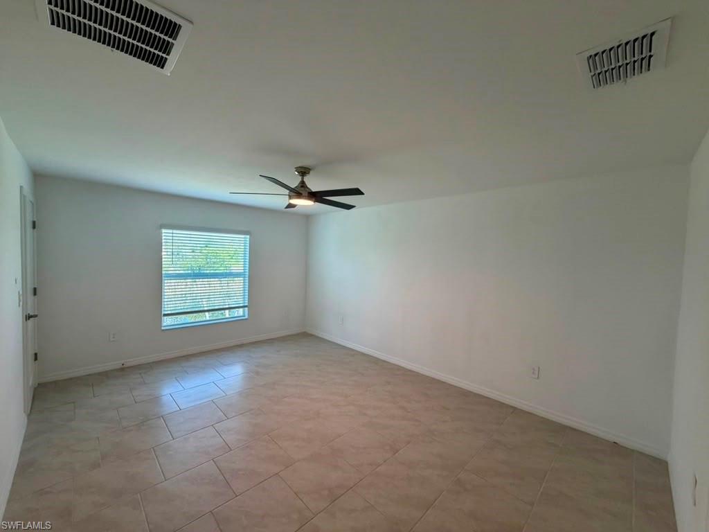 Spacious room featuring neutral-toned tile flooring, a window with blinds, a ceiling fan with integrated lighting, and white walls