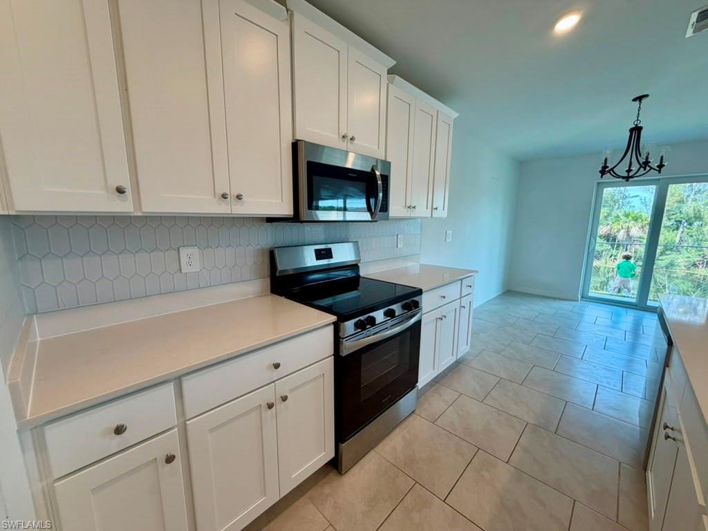 Kitchen featuring white shaker cabinetry, light-toned countertops, stainless steel appliances, and a geometric tile backsplash