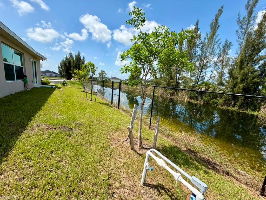 Expansive grassy yard with a black chain-link fence bordering a natural water feature