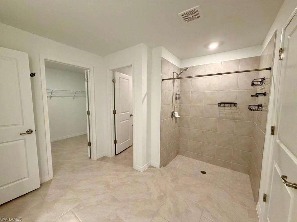 Spacious bathroom featuring large format tile flooring and a walk-in shower with tiled walls