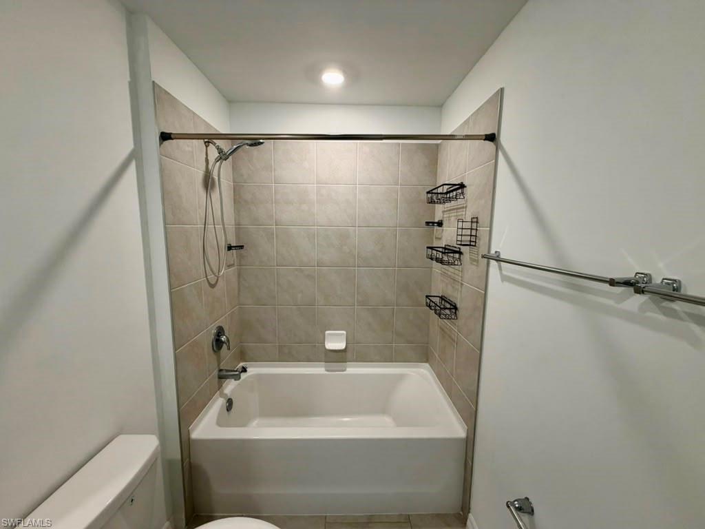 Bathtub and shower combination featuring neutral-toned tile surround, chrome fixtures, and recessed ceiling lighting