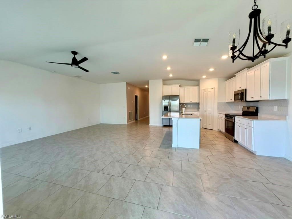 Open-concept living space featuring large format tile flooring, a modern kitchen with white cabinetry, stainless steel appliances, a center island, and recessed lighting