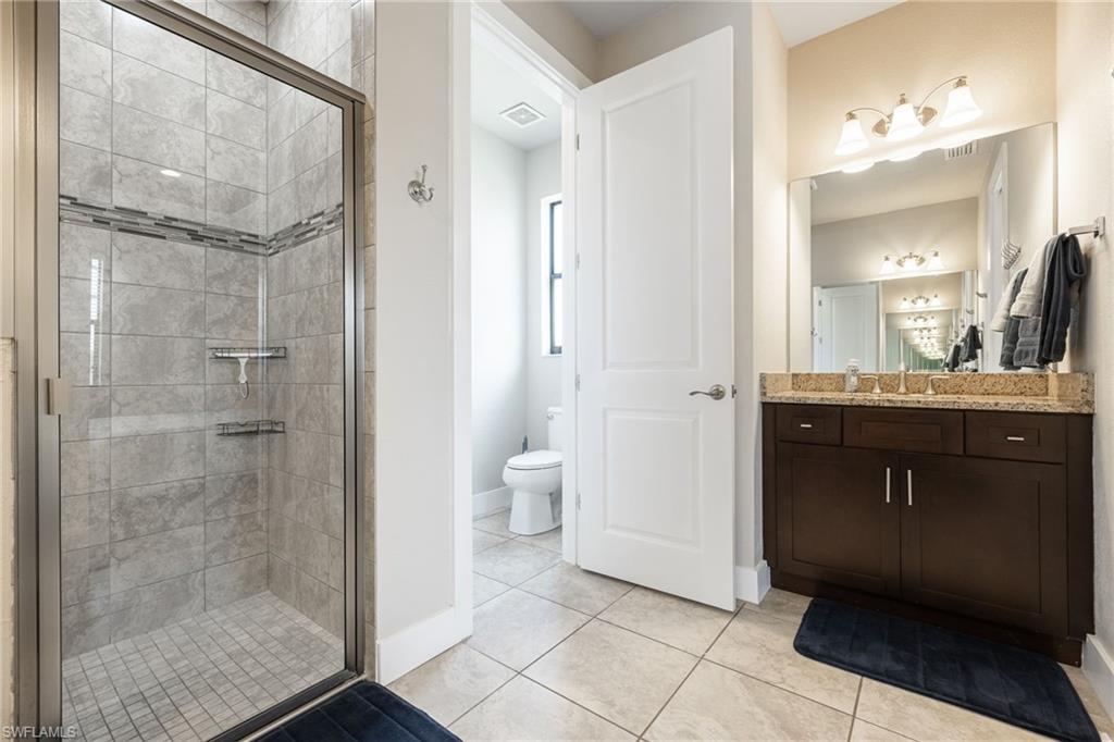 Bathroom featuring a glass-enclosed shower with tile surround, a dark wood vanity with a granite countertop, and tile flooring
