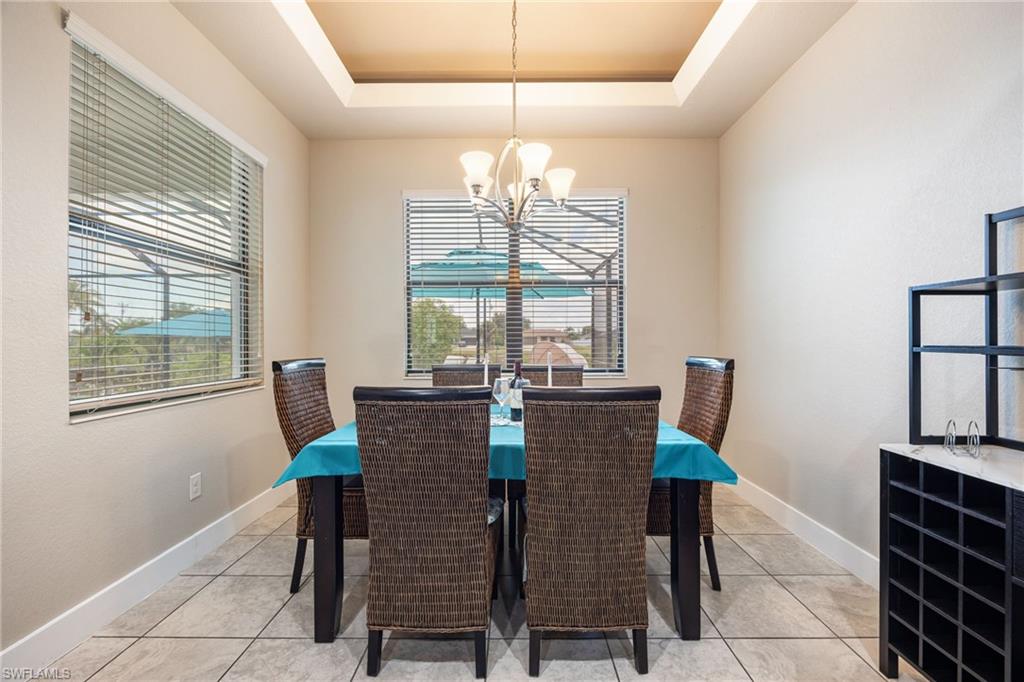 Recessed tray ceiling with central chandelier, tile flooring, and two large windows with blinds