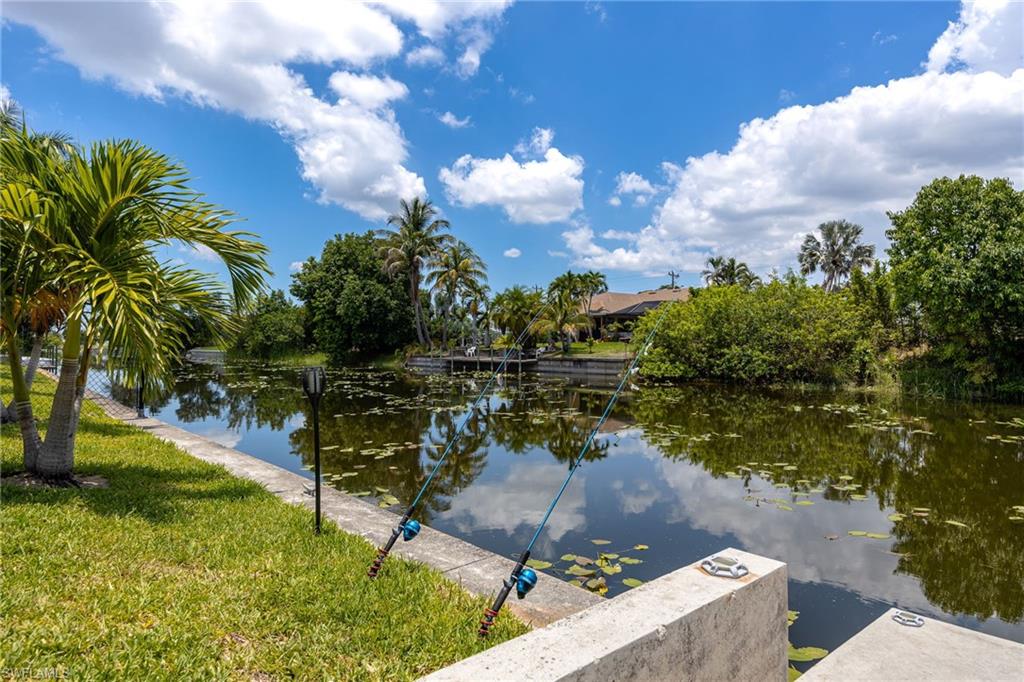 Waterfront property featuring a canal, concrete seawall, and established palm trees