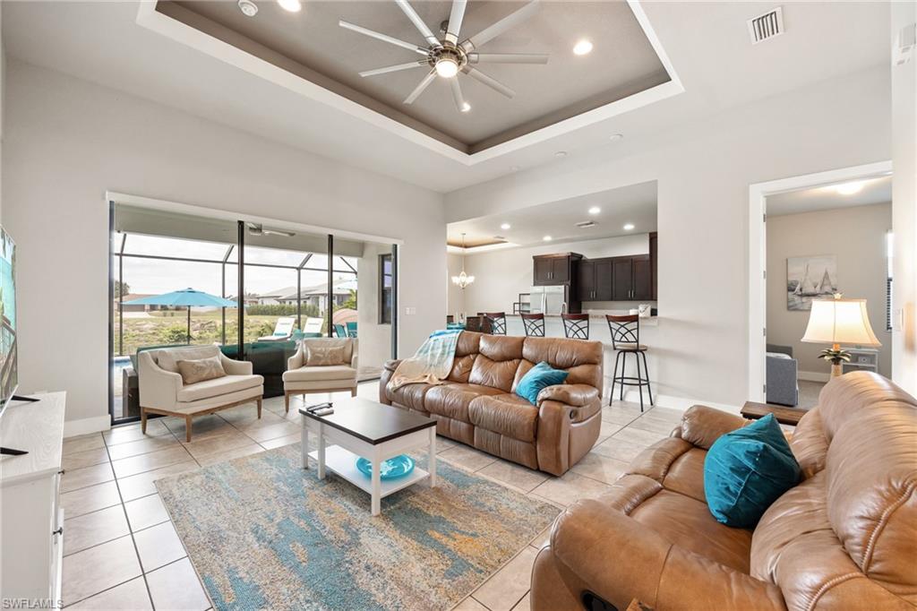 Spacious living area featuring large format tile flooring, a tray ceiling with recessed lighting and a ceiling fan, and sliding glass doors opening to a screened outdoor area