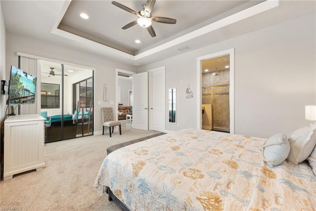 Spacious bedroom with light gray walls, plush carpet flooring, and a tray ceiling featuring recessed lighting and a ceiling fan