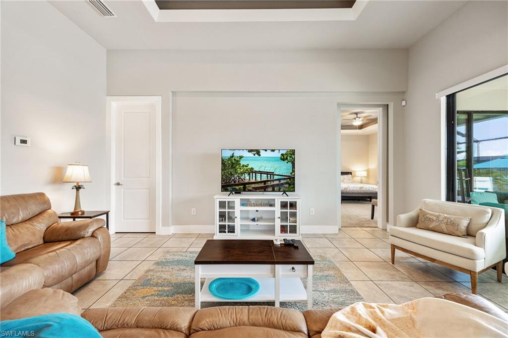 Spacious living area featuring neutral tile flooring, a tray ceiling with dark accent, and a large sliding glass door