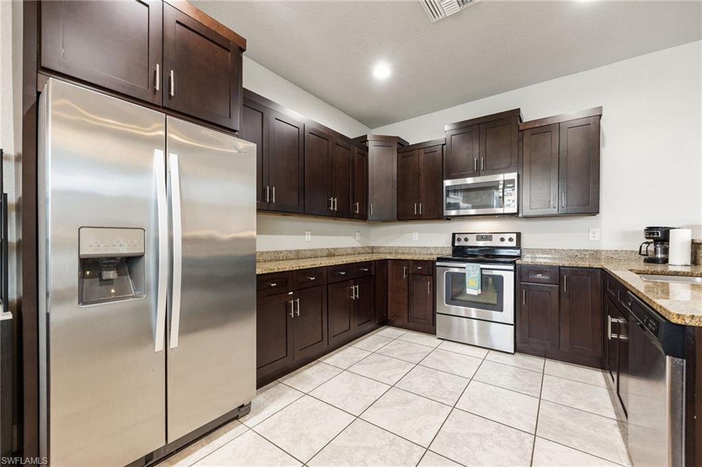 Kitchen featuring dark wood cabinetry, granite countertops, white tile flooring, and stainless steel appliances including a side-by-side refrigerator, range, microwave, and dishwasher