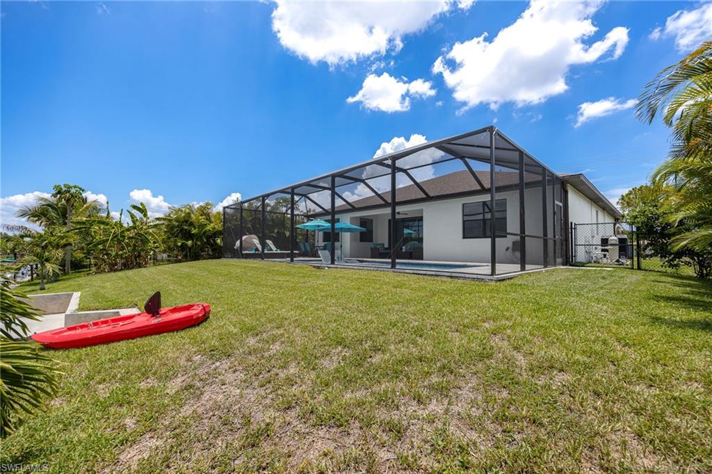 Expansive outdoor space featuring a screened-in pool area, a large grassy yard, and mature tropical landscaping