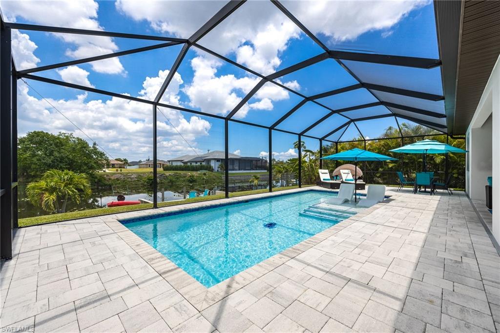 Screened-in outdoor living space featuring a rectangular swimming pool with steps, surrounded by light-toned paver decking