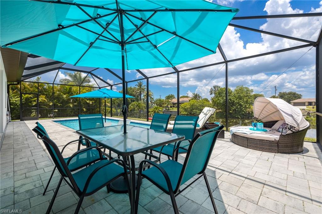 Screened outdoor living area featuring a rectangular swimming pool, paver patio, and mature tropical landscaping