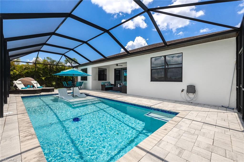 Screened-in outdoor living space featuring a rectangular pool with integrated steps, light-toned paver decking, and a white stucco exterior wall