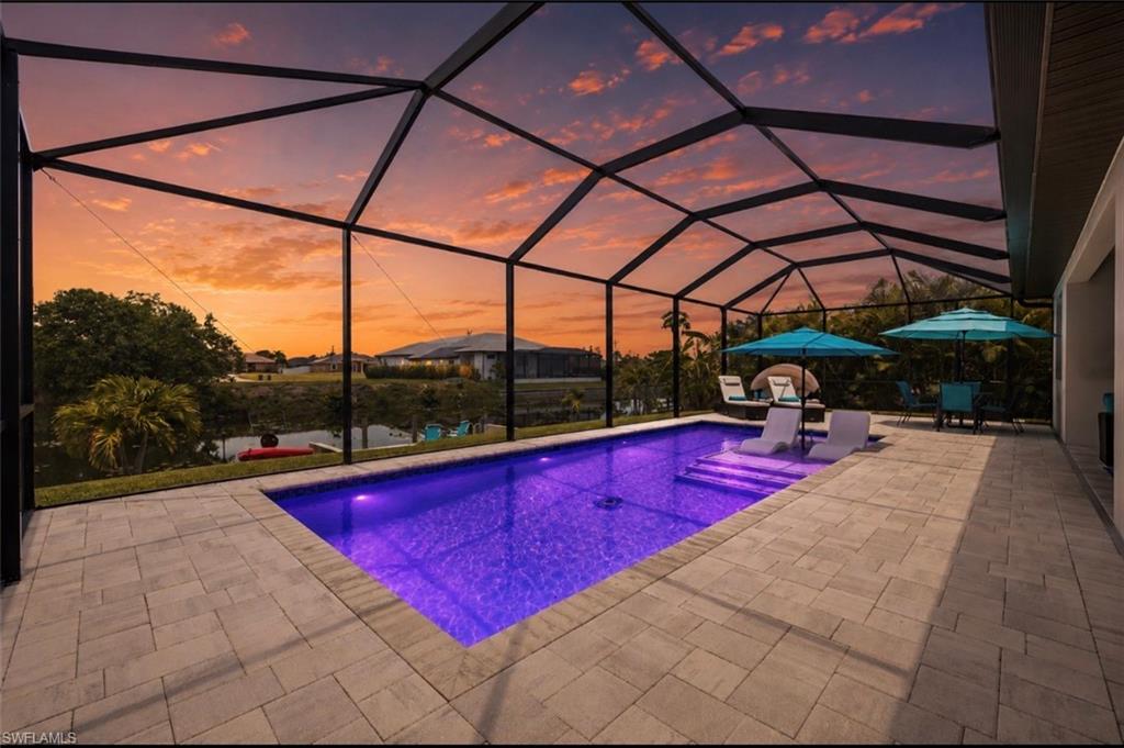 Screened lanai featuring a rectangular pool with integrated lighting, paver decking, and a stucco exterior wall