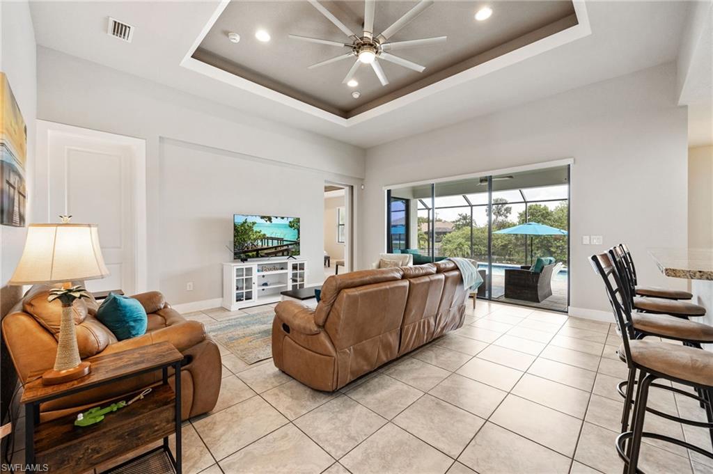 Expansive living area with large format tile flooring and a tray ceiling featuring recessed lighting