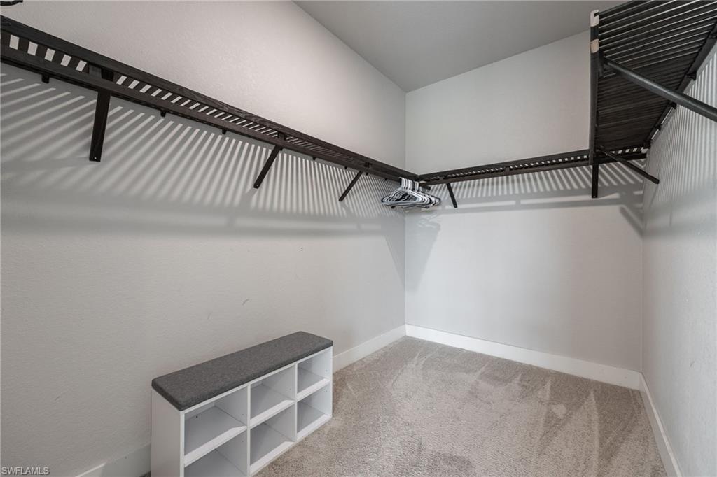 Walk-in closet featuring built-in shelving, hanging rods, light gray walls, white baseboards, and neutral carpet flooring