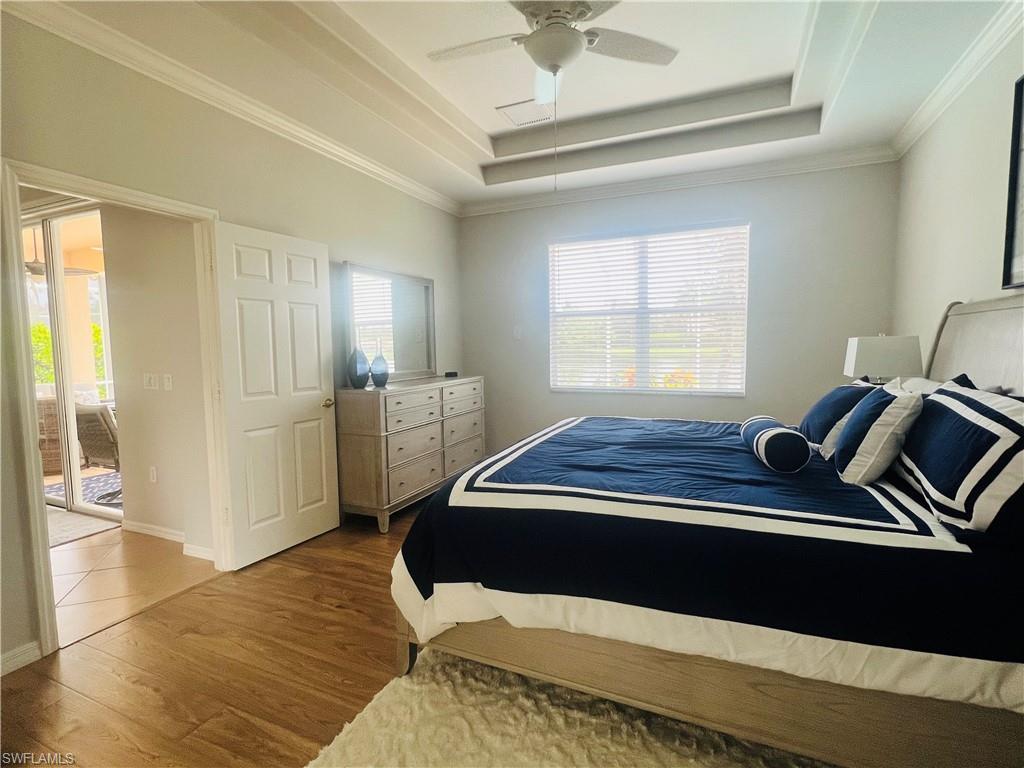 Bedroom with ceiling fan, hardwood / wood-style flooring, multiple windows, and a tray ceiling
