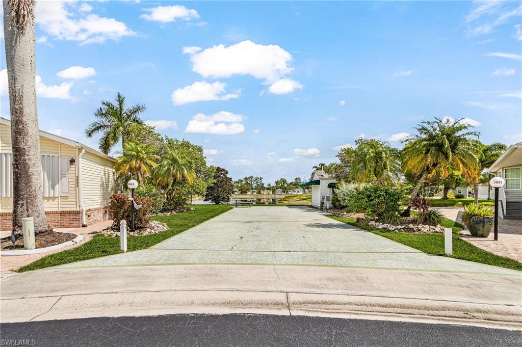 Concrete lot framed by manicured lawns and tropical landscaping, with waterfront view.
