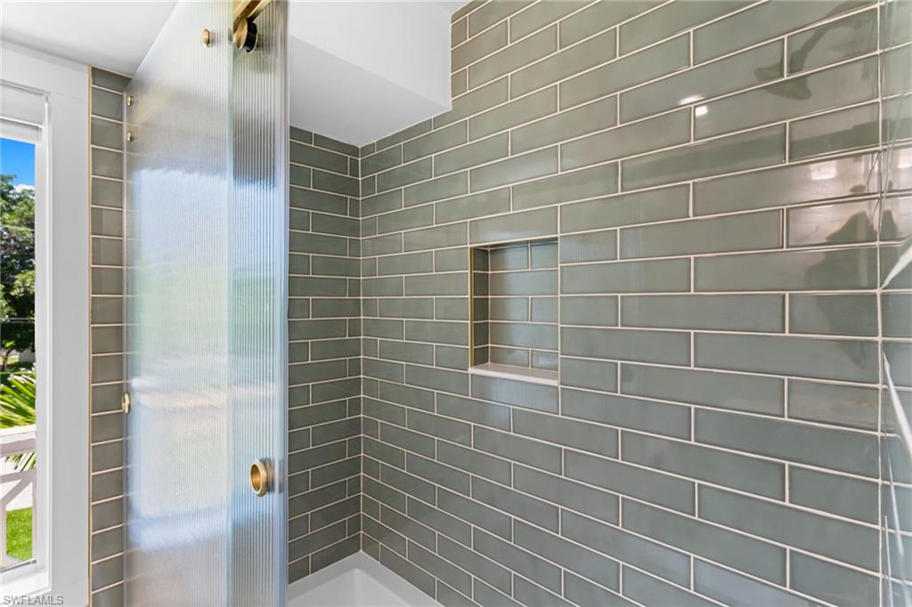 Shower enclosure featuring sleek subway tile, a built-in niche, and a fluted glass door with brass hardware