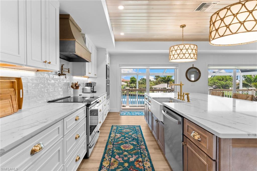 Gourmet kitchen featuring a large central island with a farmhouse sink and brass faucet, white shaker cabinetry, stainless steel appliances, and wood-finish flooring
