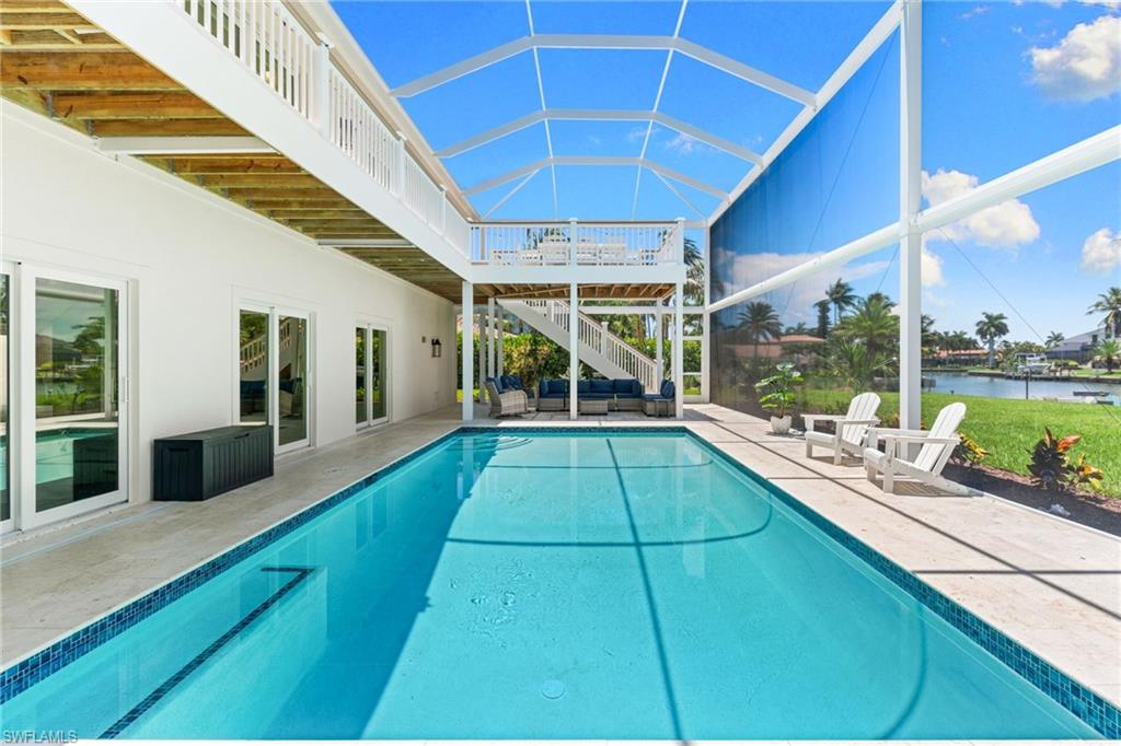 Screened-in swimming pool enclosure featuring a rectangular pool with mosaic tile trim, multiple sliding glass doors providing interior access, an upper-level balcony, and a waterfront setting