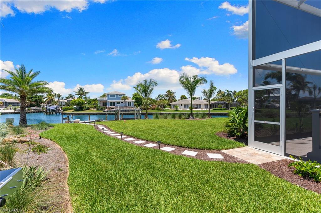Expansive waterfront property featuring a lush green lawn, mature palm trees, and a stone pathway