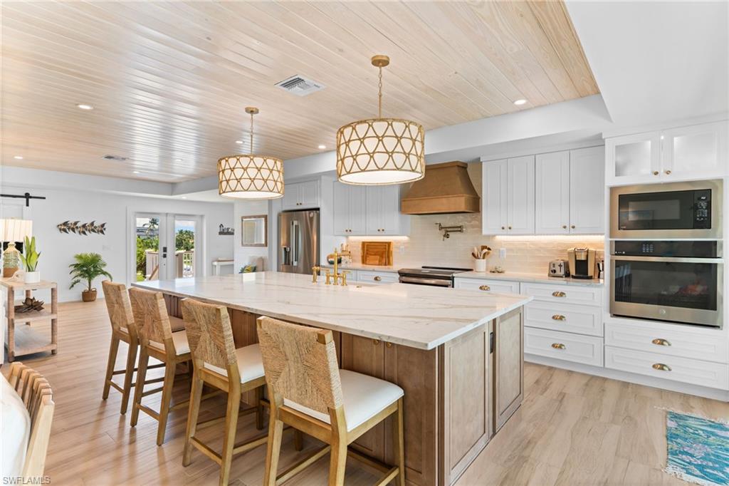 Open-concept kitchen featuring white shaker cabinetry, an expansive island with a stone countertop, stainless steel appliances, and wood-finish flooring