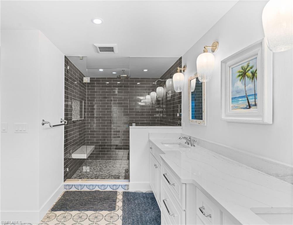 Spacious bathroom featuring a glass-enclosed shower with dark subway tile, a built-in shower bench, and a dual vanity with white countertops and undermount sinks